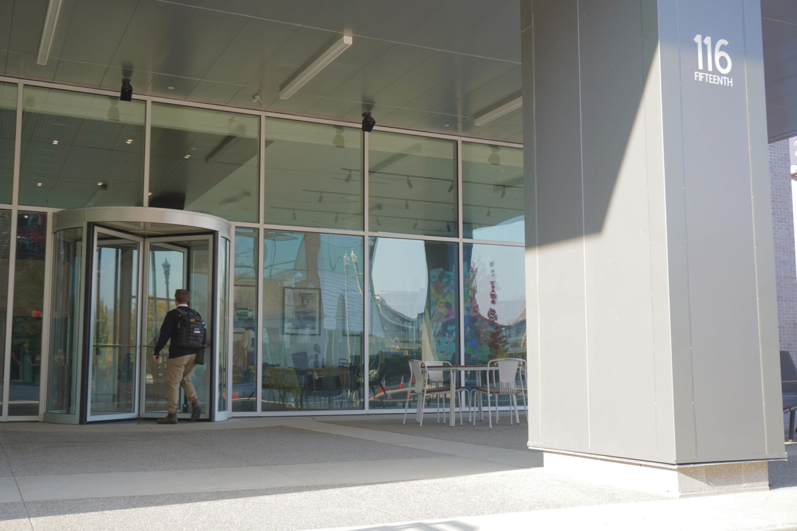 A person with a backpack enters a building through a revolving door, with โ116 FIFTEENTHโ printed on a gray pillar in the foreground.