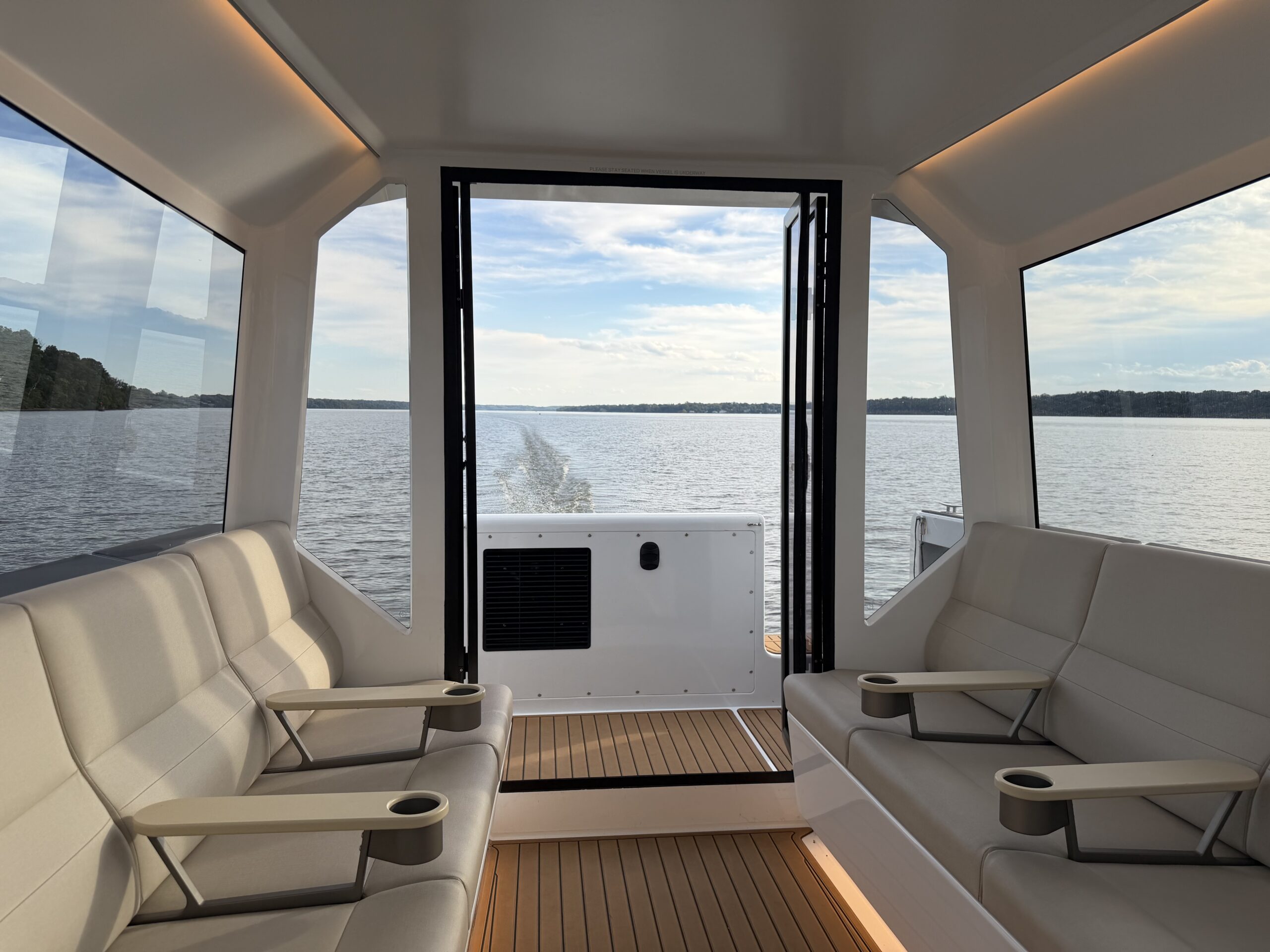 View from inside a boat cabin looking out through an open rear door toward a calm lake.