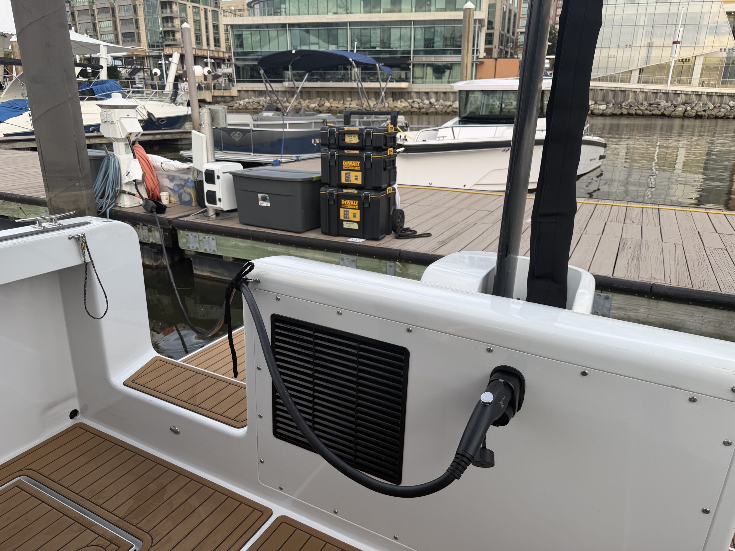 A charging cable plugged into a white boat deck, with a marina and docked boats in the background.