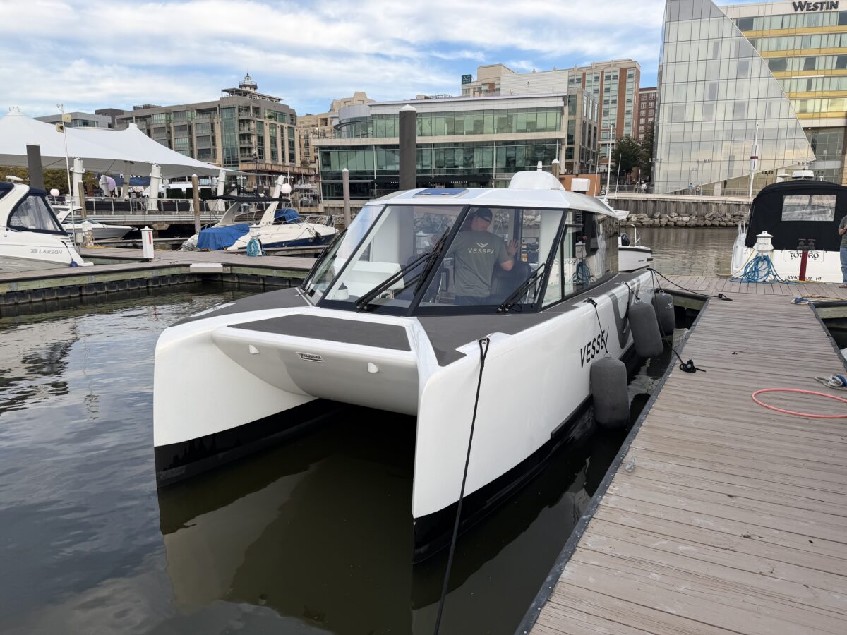A modern white catamaran motorboat labeled “VESSEV” docked at a wooden pier in a marina.