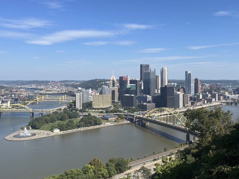 High-angle view of the Pittsburgh skyline at the confluence of three rivers, featuring bridges and Point State Park.