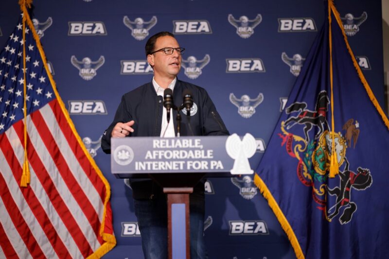 Pennsylvania Governor Josh Shapiro speaks at a podium with a sign that reads “Reliable, Affordable Internet for PA,” flanked by the US and Pennsylvania state flags.