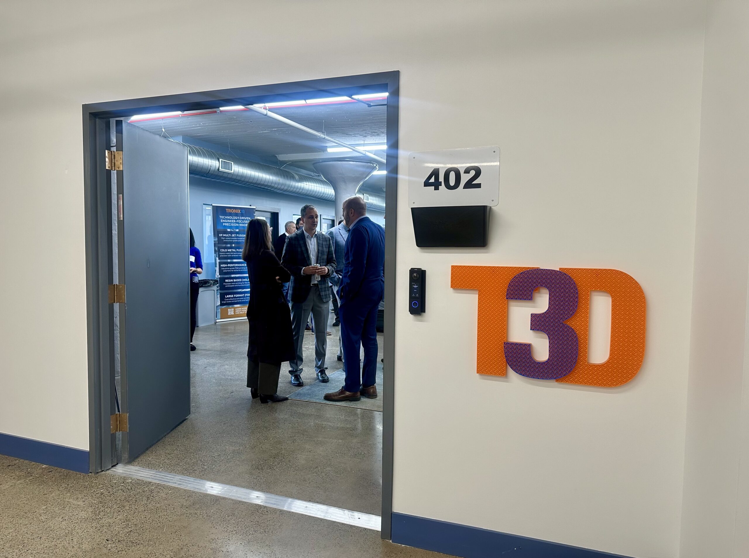 People standing in the doorway of a room marked โ402โ with a โT3Dโ sign on the wall.
