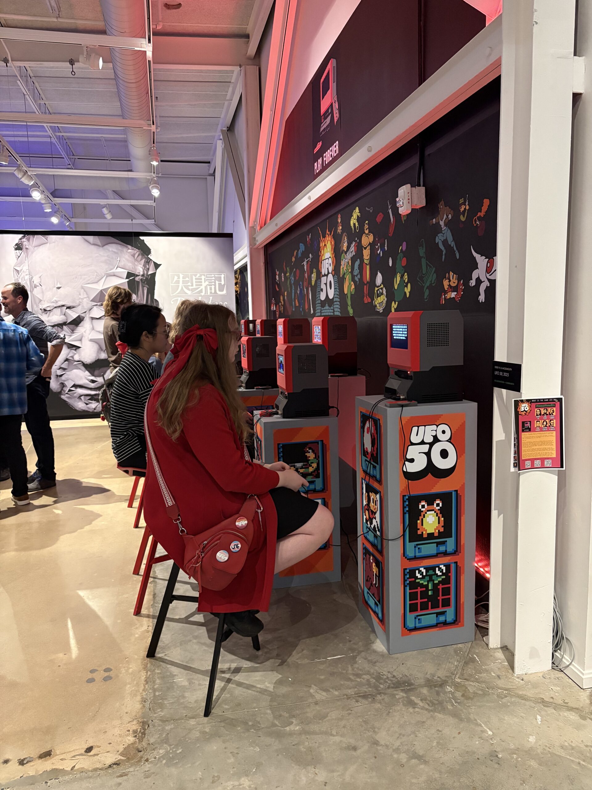 People sitting on stools playing UFO 50 video games at a gaming exhibition.