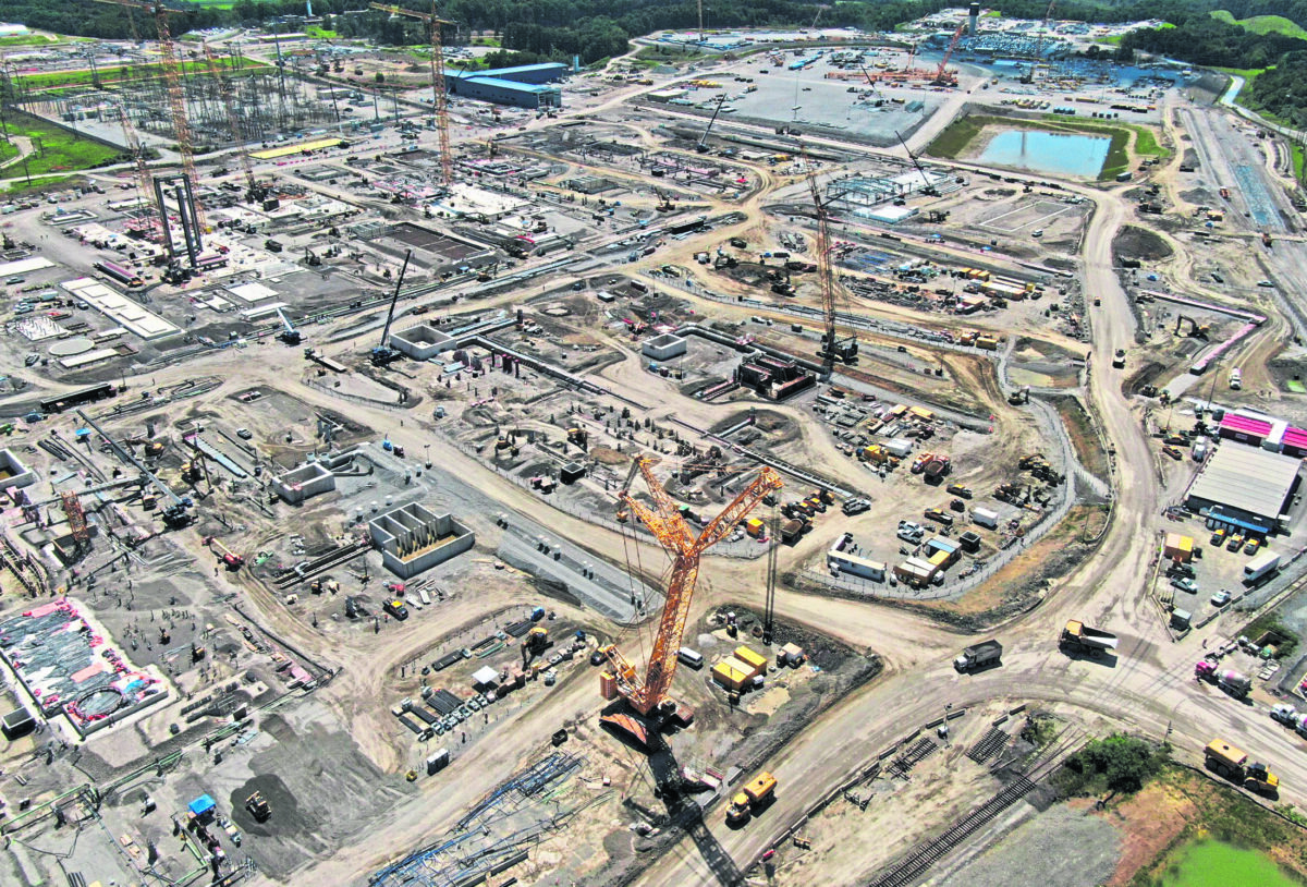 Aerial view of a large, active construction site with multiple cranes, earth-moving equipment, and foundation structures.