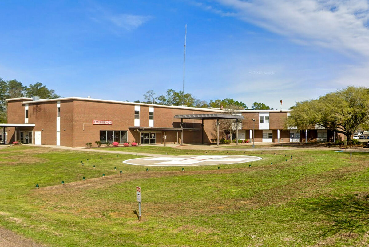 A brick hospital building with an emergency entrance and a helipad on the front lawn.