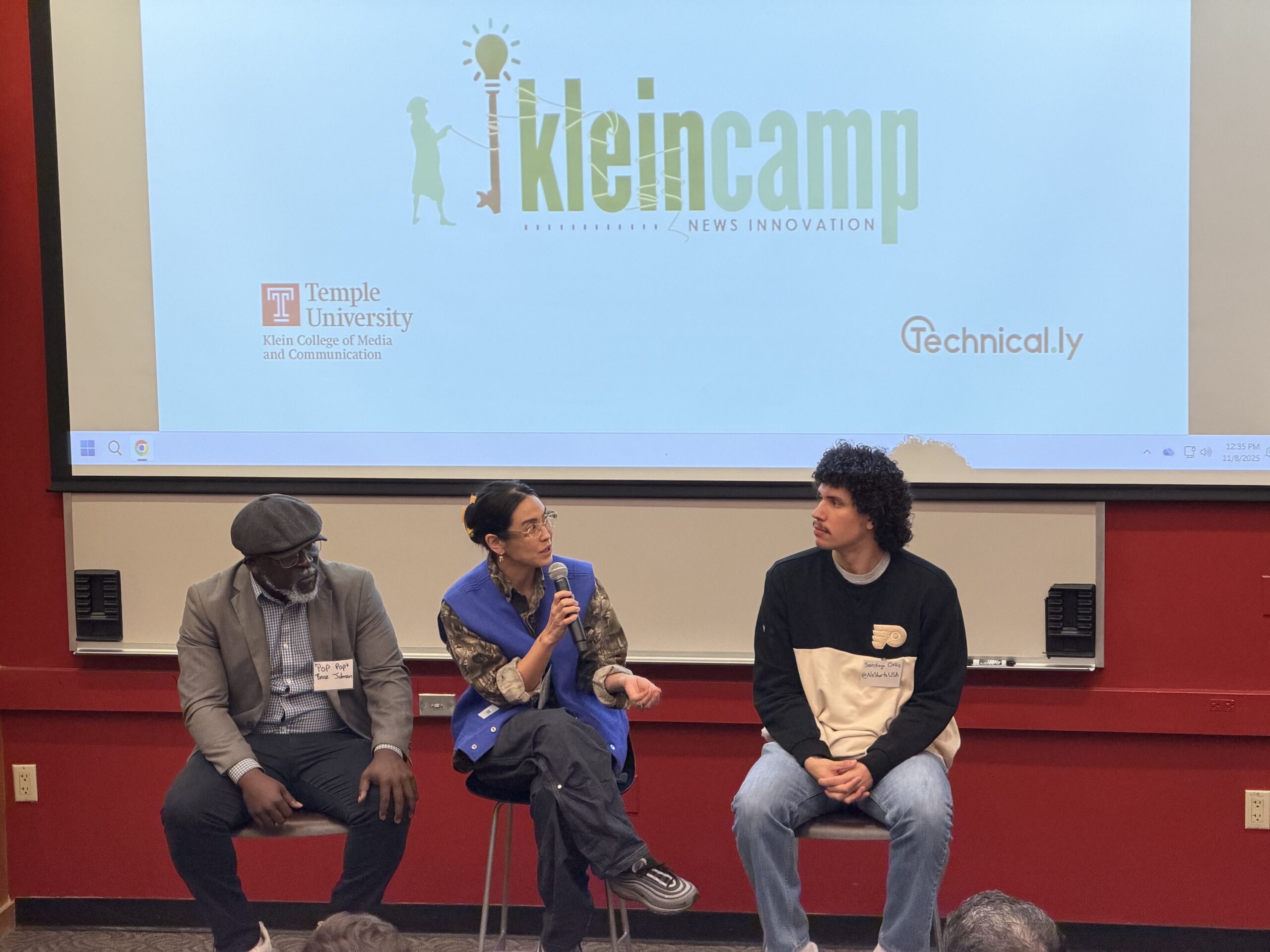 Three people sit on stools on a stage in front of a screen displaying a “kleincamp” logo.