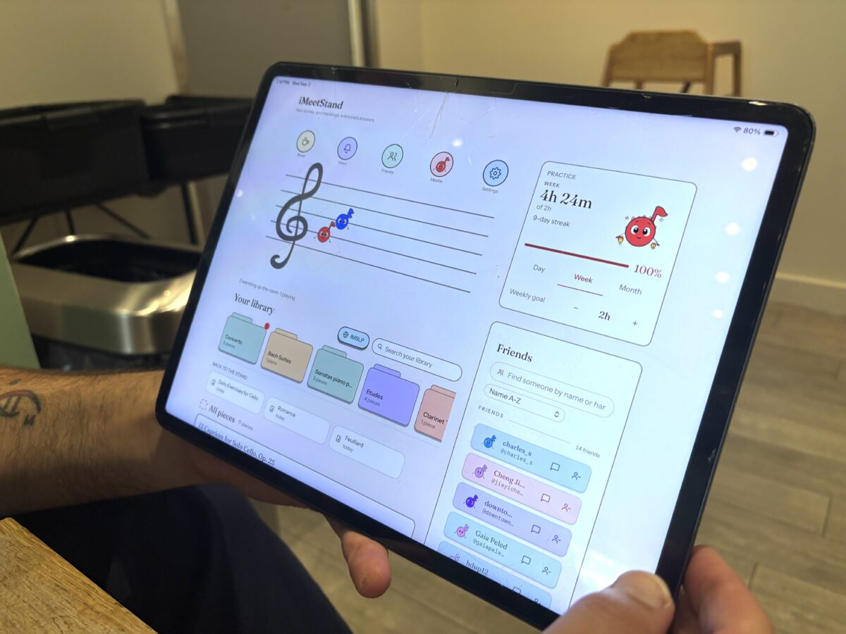 A person holding a tablet displaying the iMeetStand music app dashboard, showing practice statistics, a music library, and a friends list.