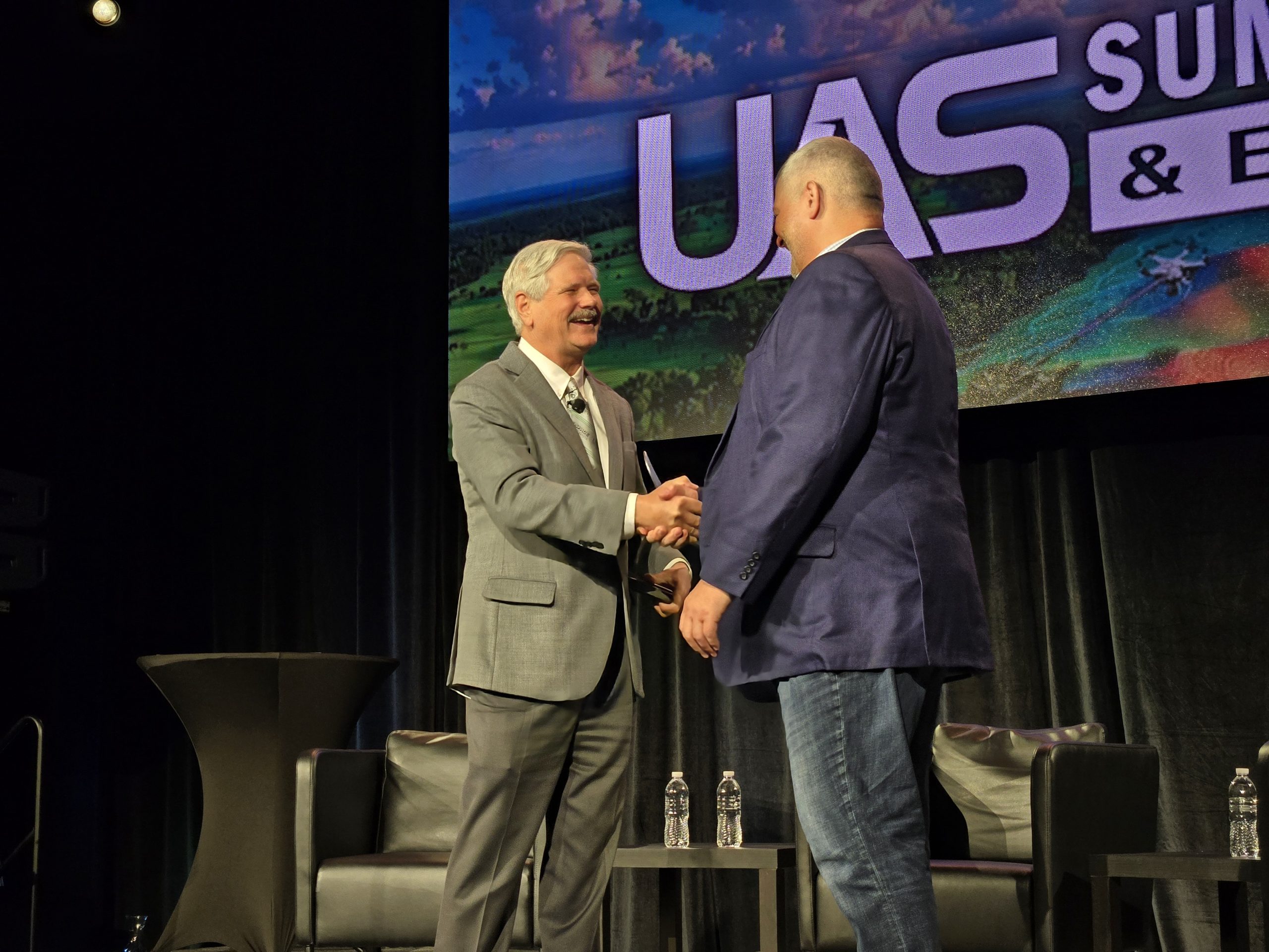Senator John Hoeven and GrandSKY founder and president Tom Swoyer shake hands on stage at the 2026 UAS Summit & Expo. 